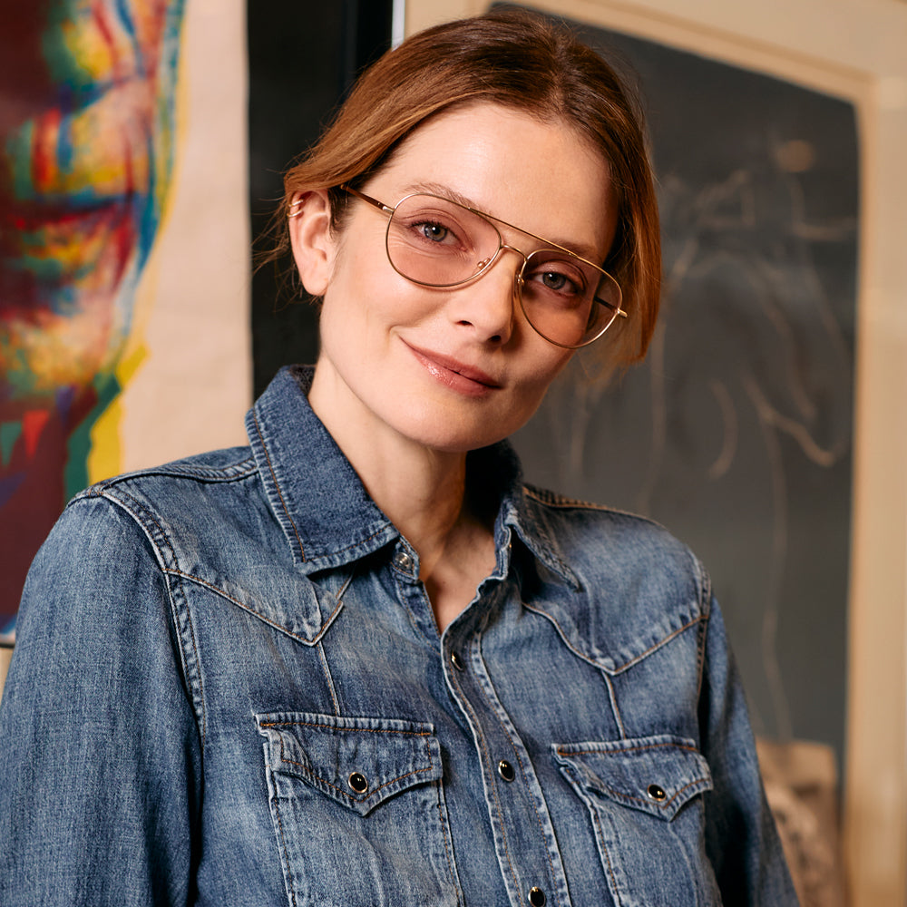 A person is wearing gold aviator glasses with a pink tint.