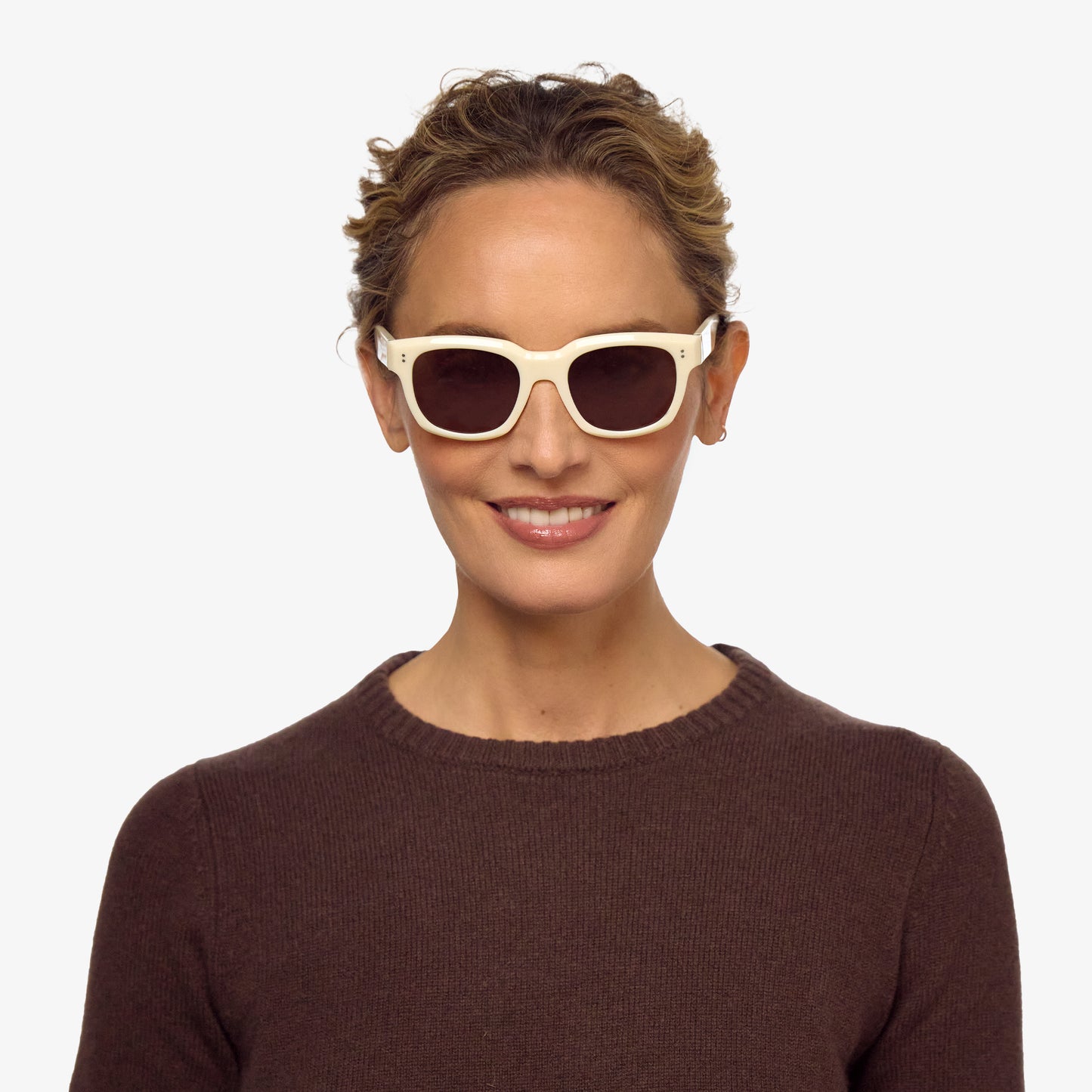 A person wears square glasses with a shiny bone coloured frame and dark brown tinted lenses.