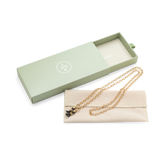 A gold chain rests on a cream colored case beside an open pale green box.