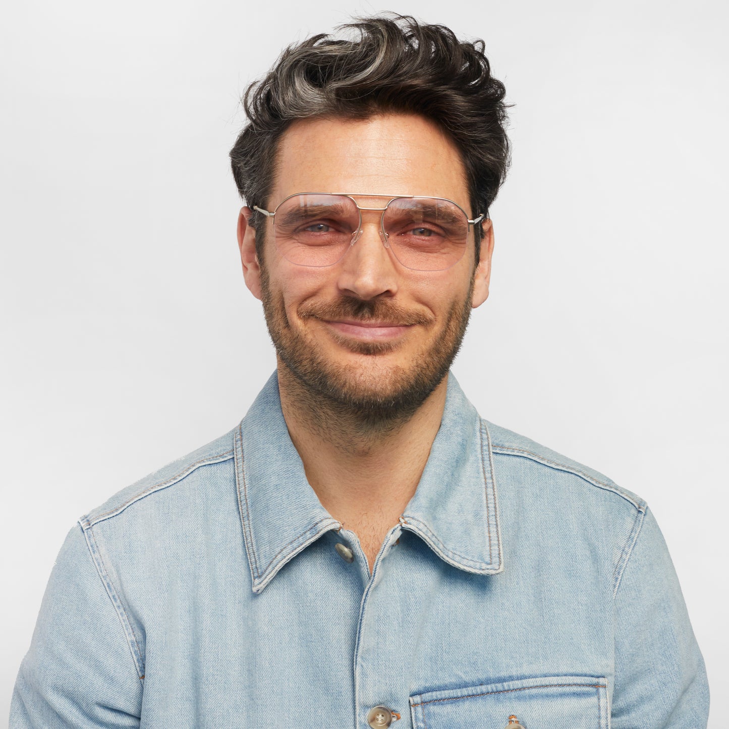 A person wears square glasses with a gold frame and pink tinted lenses.
