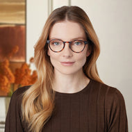 
A person wears round tortoise finish frames with clear lenses.