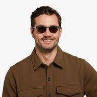 
A person is wearing round sunglasses with shiny aqua frames and dark brown tinted lenses.