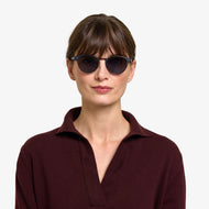 
A person wears round dark tortoise finish frames with dark tinted lenses.