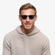 
A person wears round dark tortoise frames with dark tinted lenses.