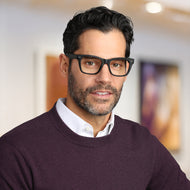 
A person is wearing square black glasses with a matte finish and clear lenses.
