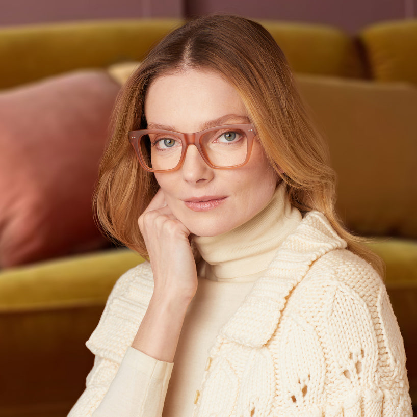 
Square champagne coloured frames with clear lenses worn by a person.