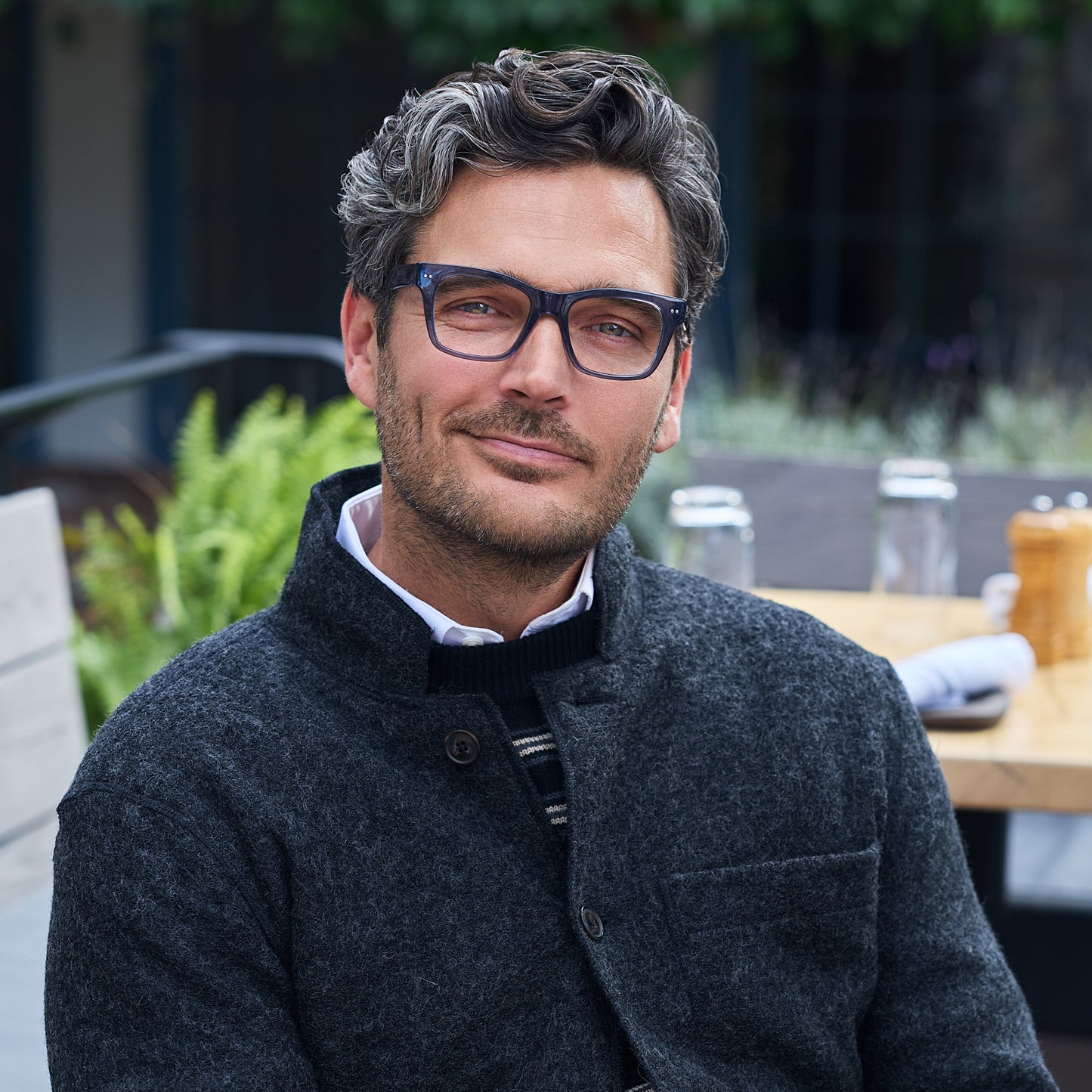 
A man wears shiny grey blue square frames with clear lenses.