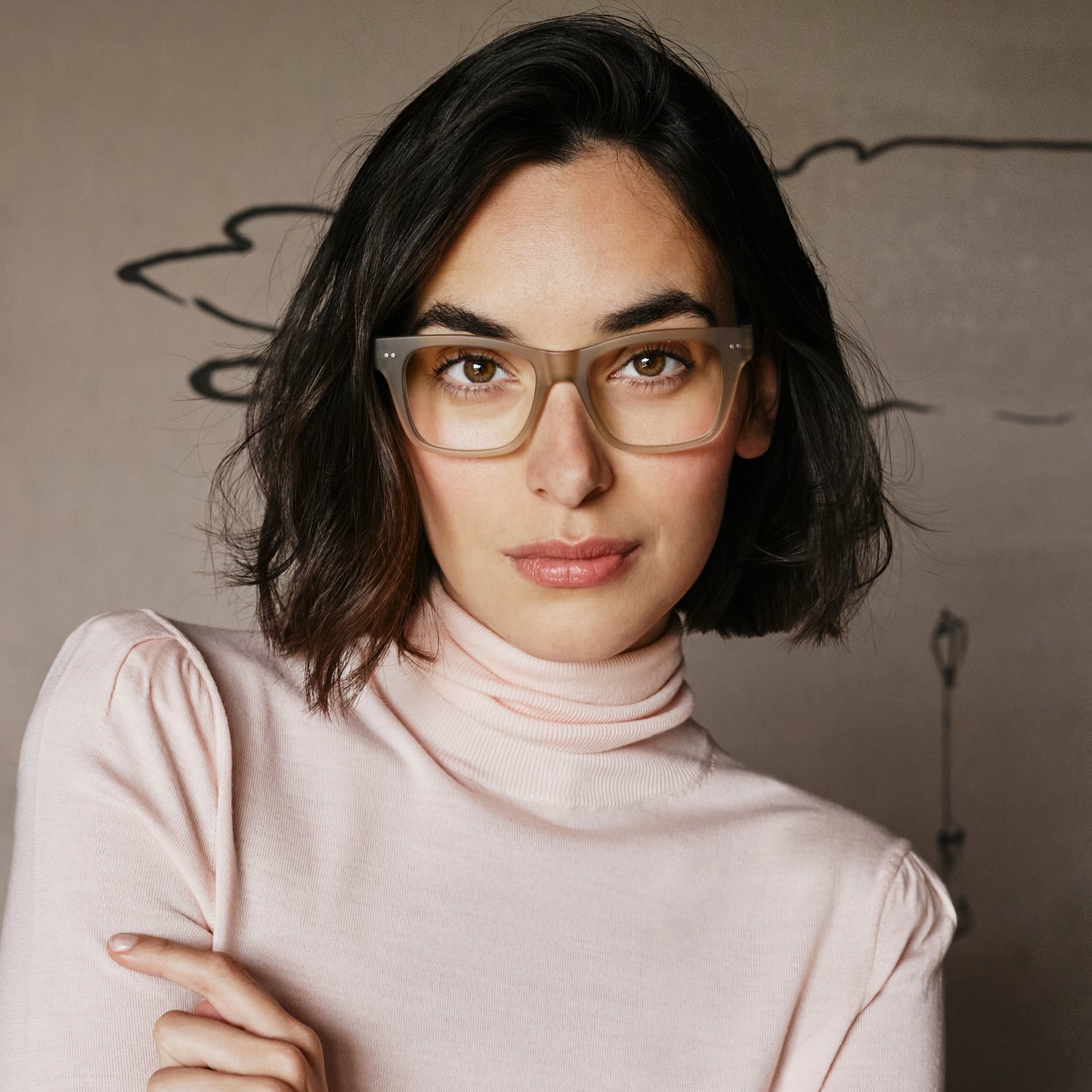 
Square taupe frames with clear lenses worn by a person.