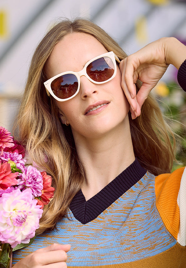 Woman wearing white cat-eye sunglasses beside a colorful bouquet of flowers.