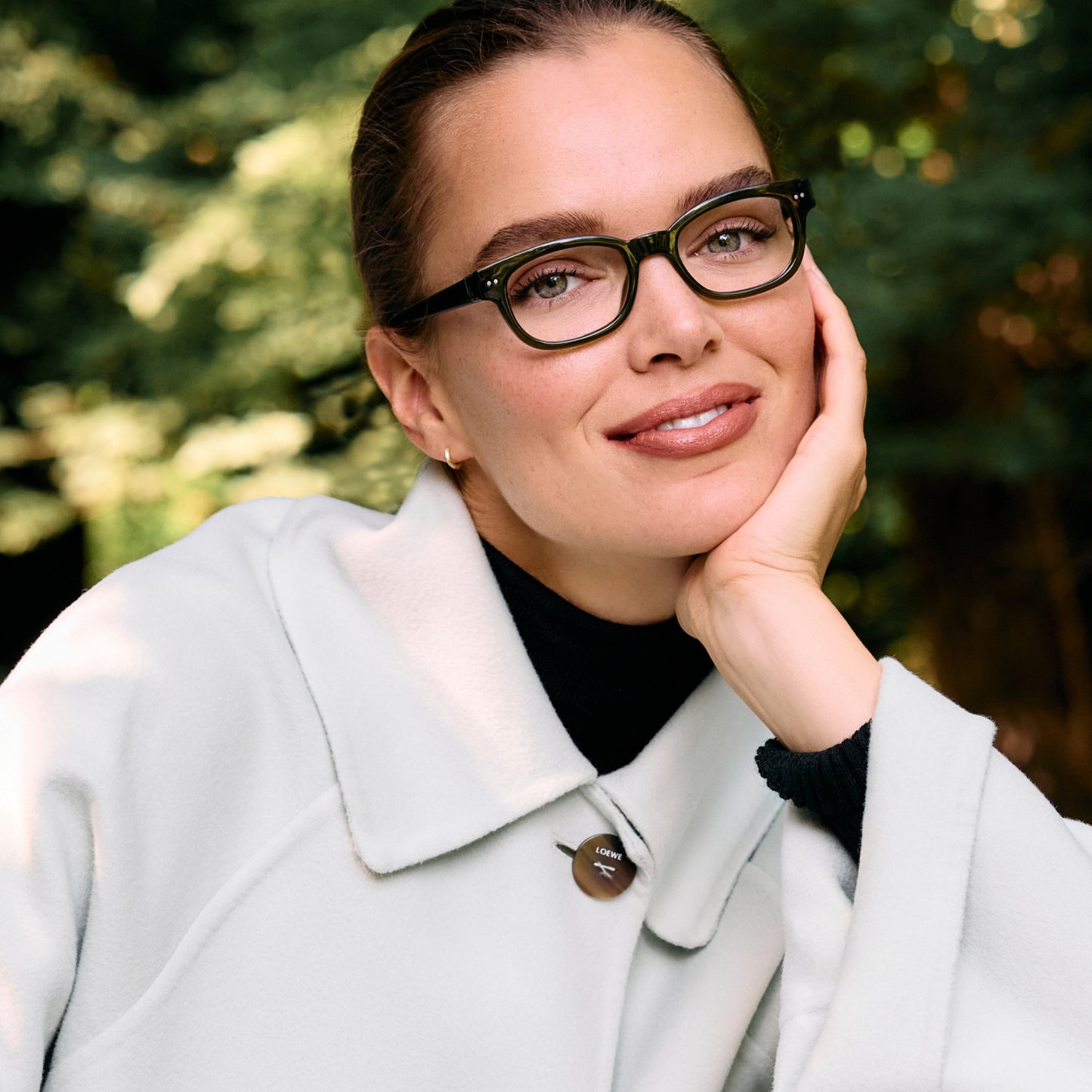 
A person is wearing shiny forest green rectangular glasses with clear lenses.