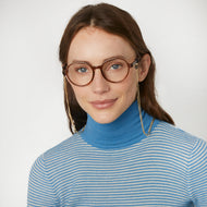 
A person wears round brown frames with a glossy finish, clear lenses, and long gold chains.