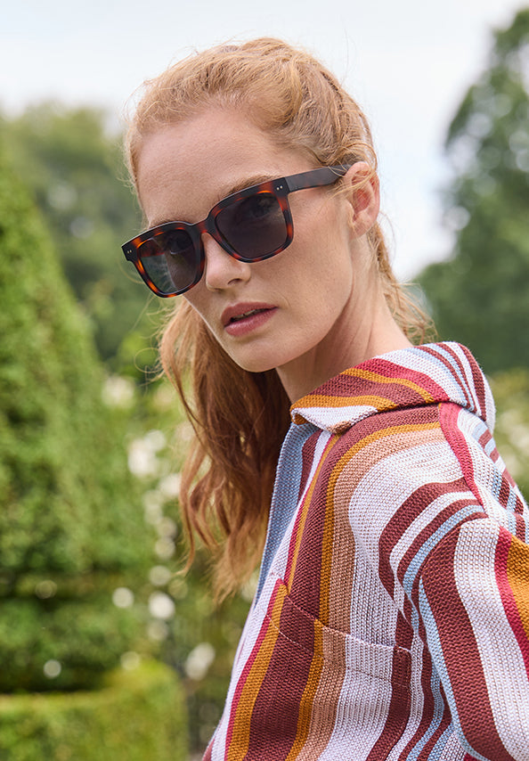 Woman wearing dark tortoiseshell sunglasses and a colorful striped shirt outdoors.
