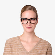 
A person wears shiny green tortoise square frames with clear lenses.