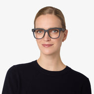 
Square navy glasses with a dark finish and clear lenses worn by a person.