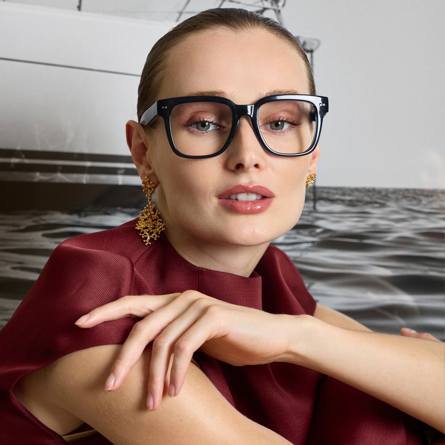 
A person wears square shiny navy frames with clear lenses.