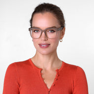 
Person wearing square taupe eyeglass frames with a translucent finish and clear lenses.