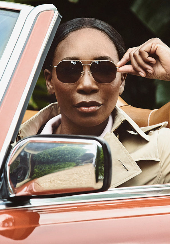 Woman wearing brown aviator sunglasses in a red convertible.
