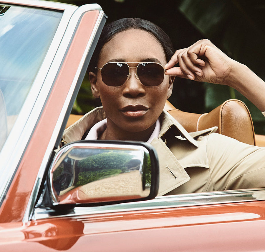Woman wearing round sunglasses seated in a vintage red convertible.