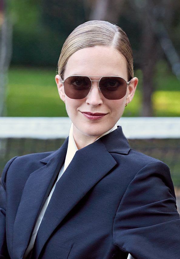 Woman wearing dark rectangular sunglasses and a navy blazer outdoors.