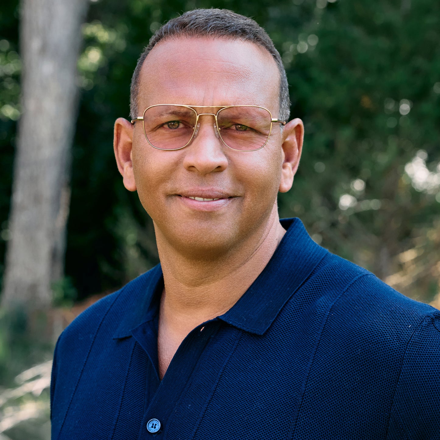 
A person in a navy polo wears gold aviator-style eyeglasses with a double bridge and light pink tinted lenses.