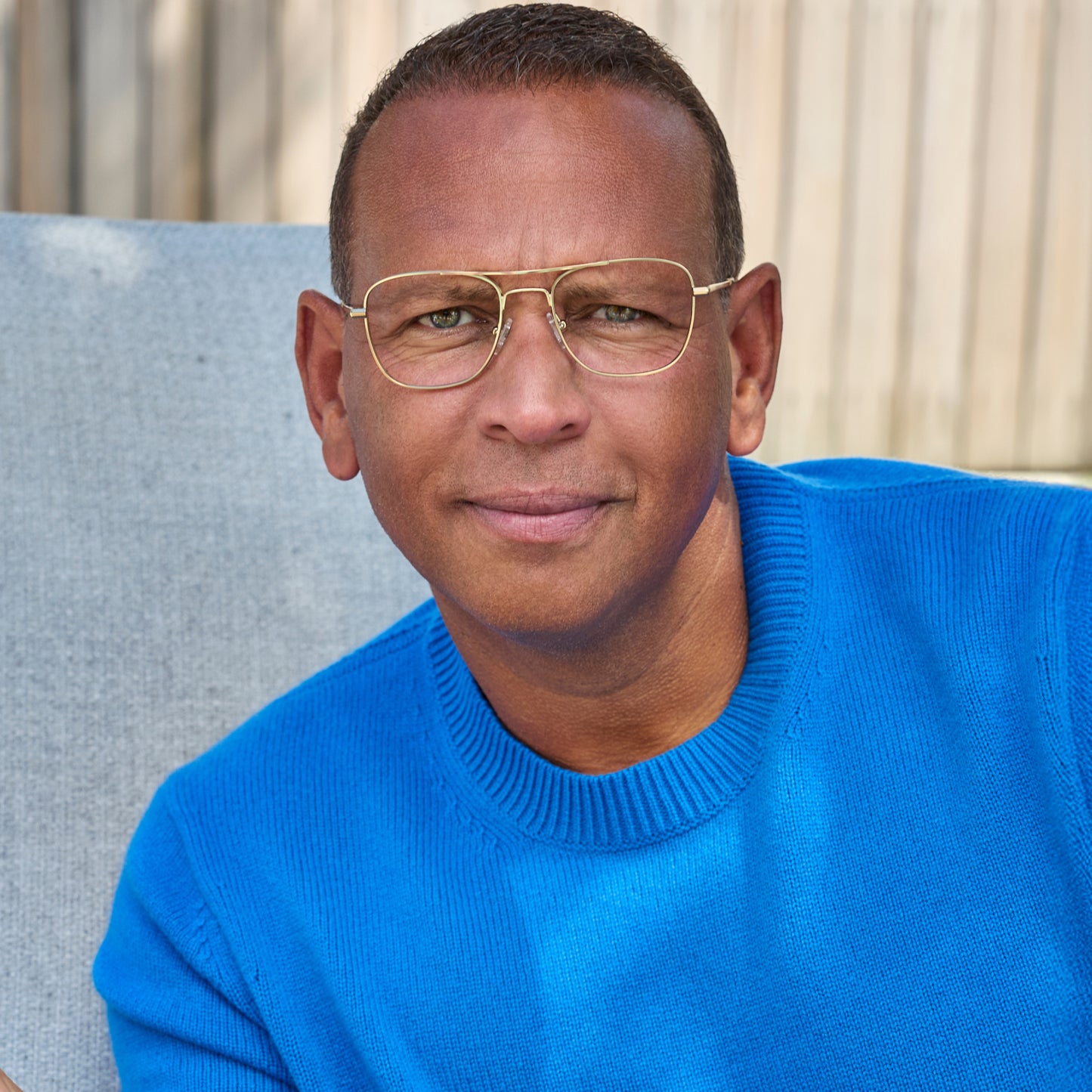 
A person in a bright blue sweater wears gold aviator-style eyeglasses with a double bridge and clear lenses.