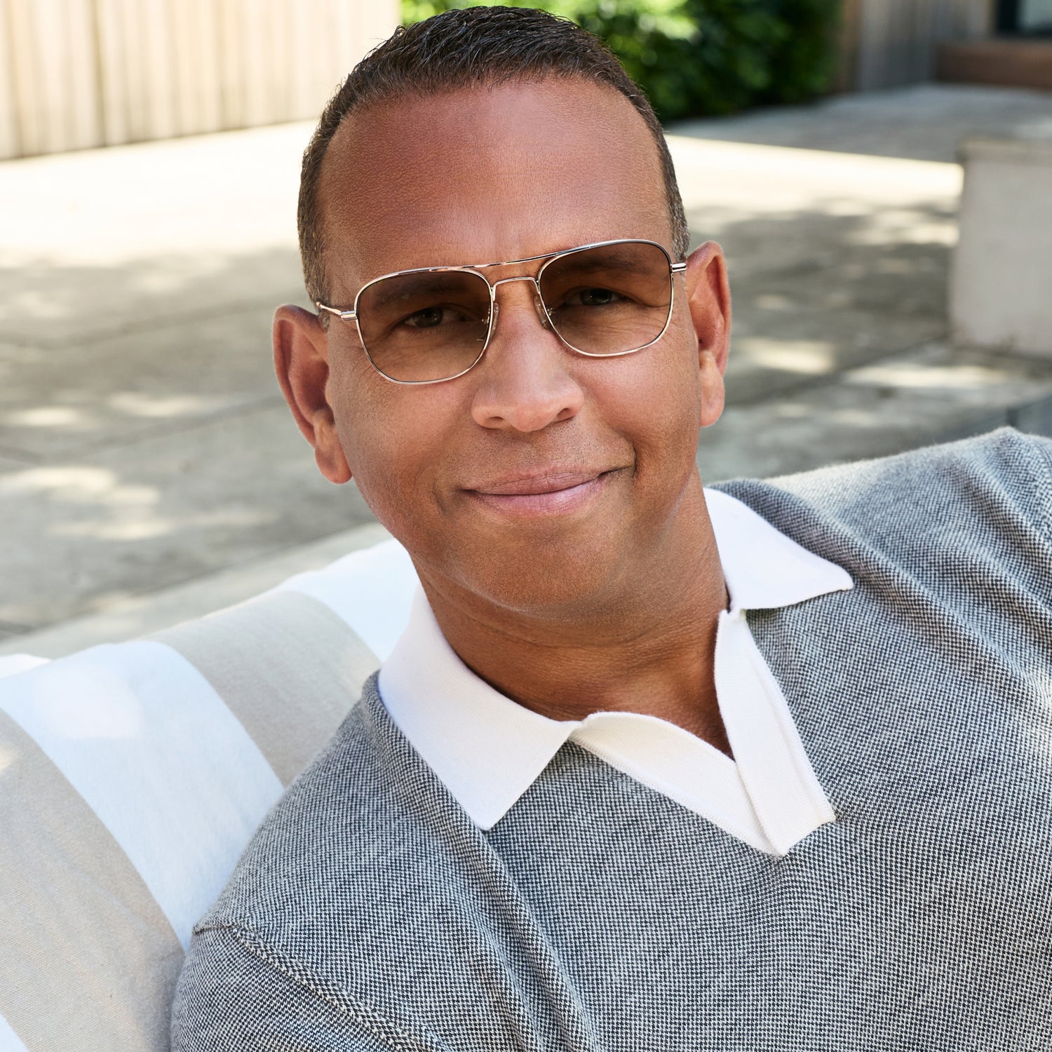 
A person in a gray knit polo wears shiny rose gold aviator-style eyeglasses with a double bridge and brown gradient tinted lenses.