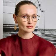 
A person in a dark red top wears gold aviator-style eyeglasses with a double bridge and clear lenses.