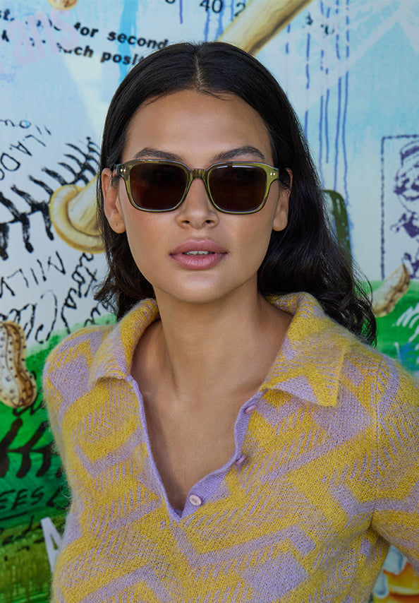 Woman wearing dark rectangular sunglasses and a yellow lavender patterned cardigan.