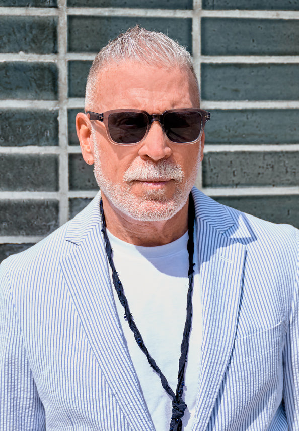 Older man wearing dark sunglasses and a blue-and-white striped blazer.