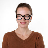 
A person is wearing shiny black rectangle frames with clear lenses.