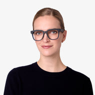 
A person wears square black frames with a glossy finish and clear lenses.