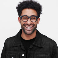 
A person wears square black eyeglass frames with clear lenses.